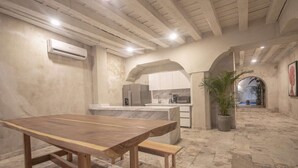 Una cocina amplia con encimera de mármol, una mesa de madera y un banco. Hay una planta en maceta y un arco que da a otra habitación.