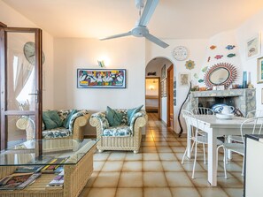 Una sala acogedora con muebles de mimbre, un comedor con sillas blancas y una chimenea con adornos.
