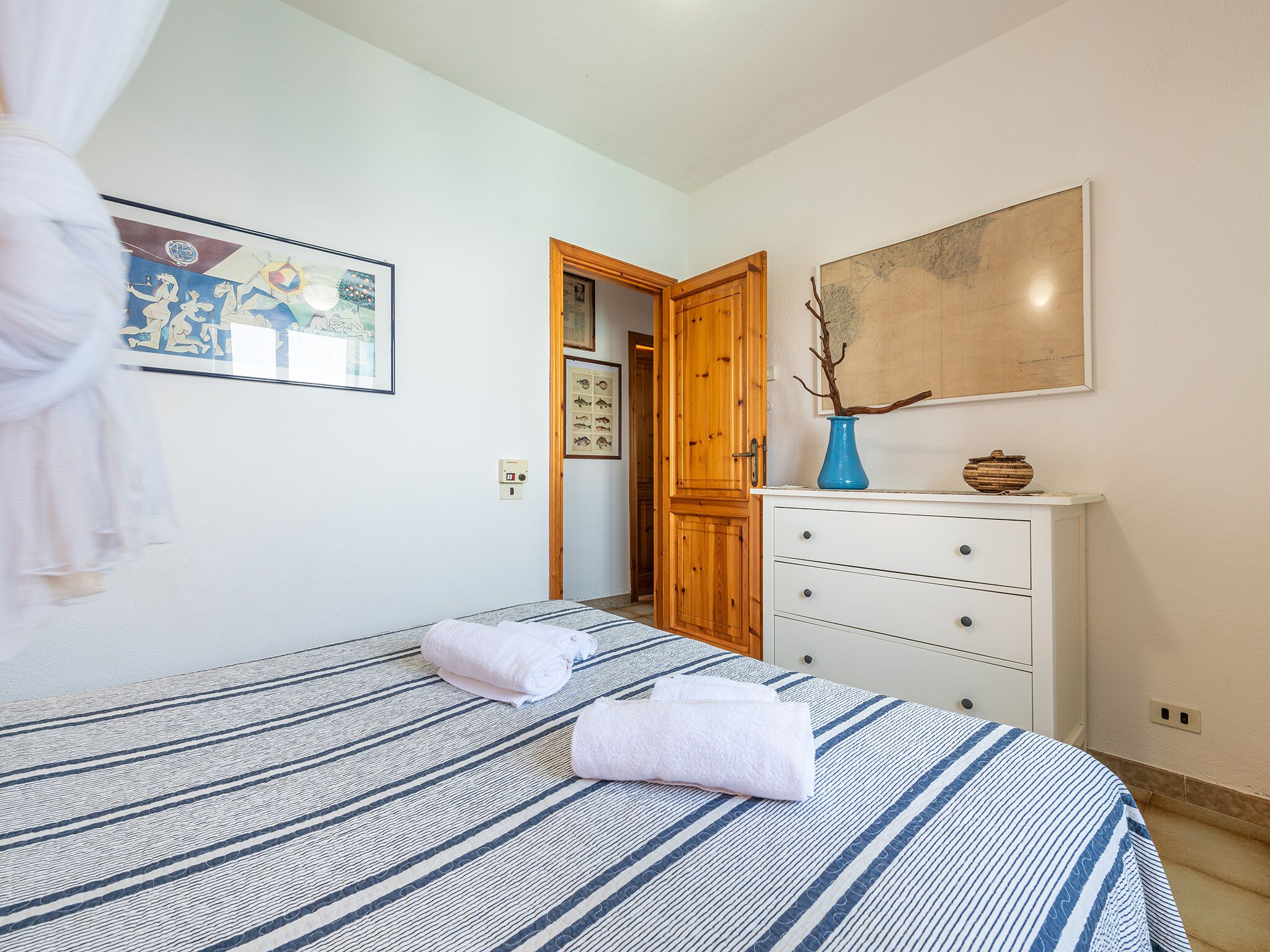 Une chambre à coucher avec un lit, une commode, un tableau et une porte donnant sur une autre pièce.