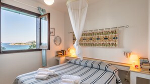 Ein Schlafzimmer mit einem Bett, Nachttischen, einem Fenster mit Meerblick und einem Himmelbett.
