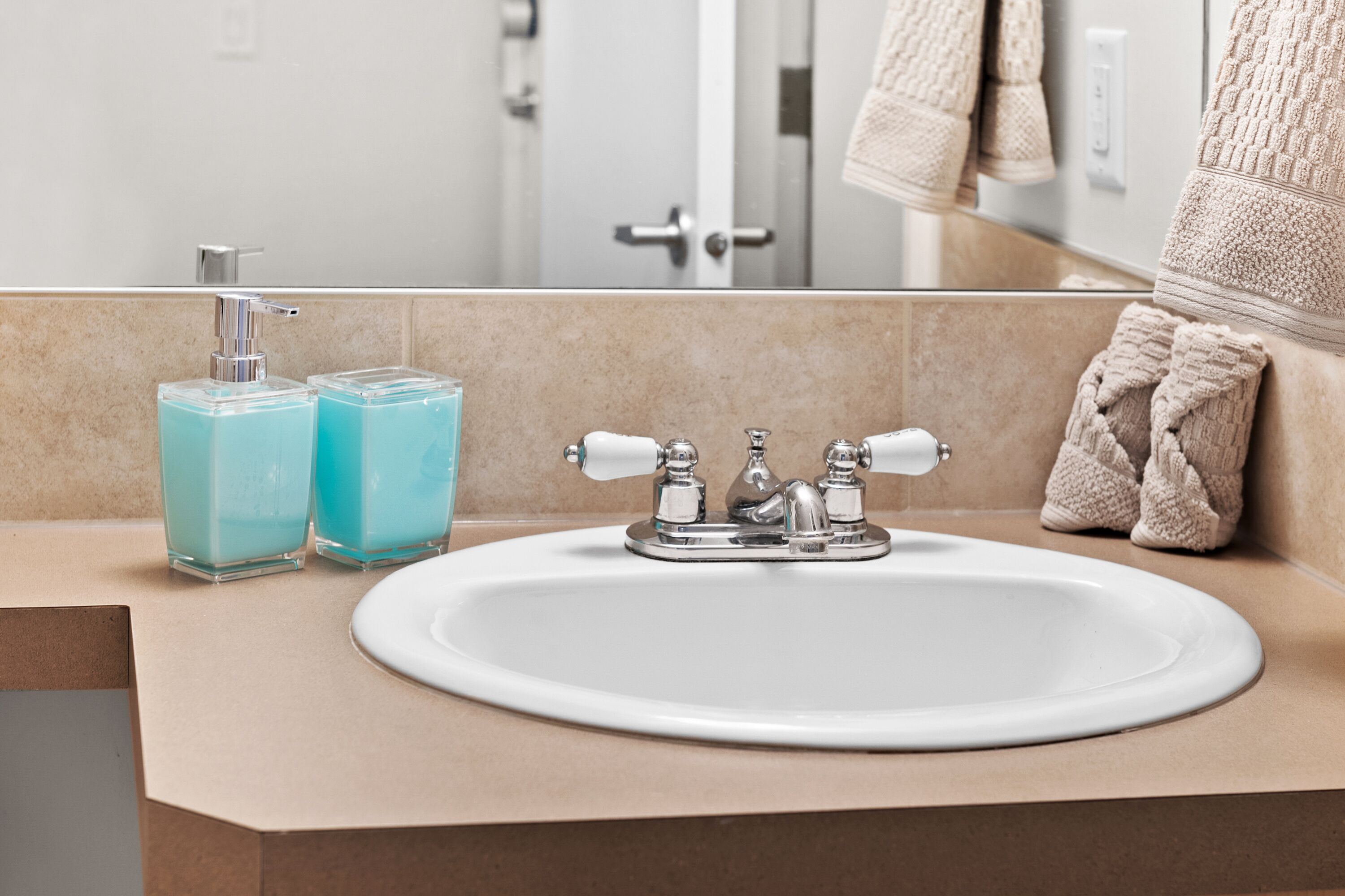A bathroom with a white sink, two blue soap dispensers, and a towel rack with a beige towel.