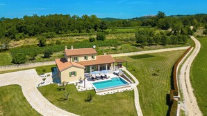 Une grande maison avec une piscine, entourée d’une pelouse bien entretenue et d’une allée pavée.