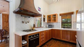 Una cocina con armarios de madera, estufa a gas, microondas y una ventana con persianas.