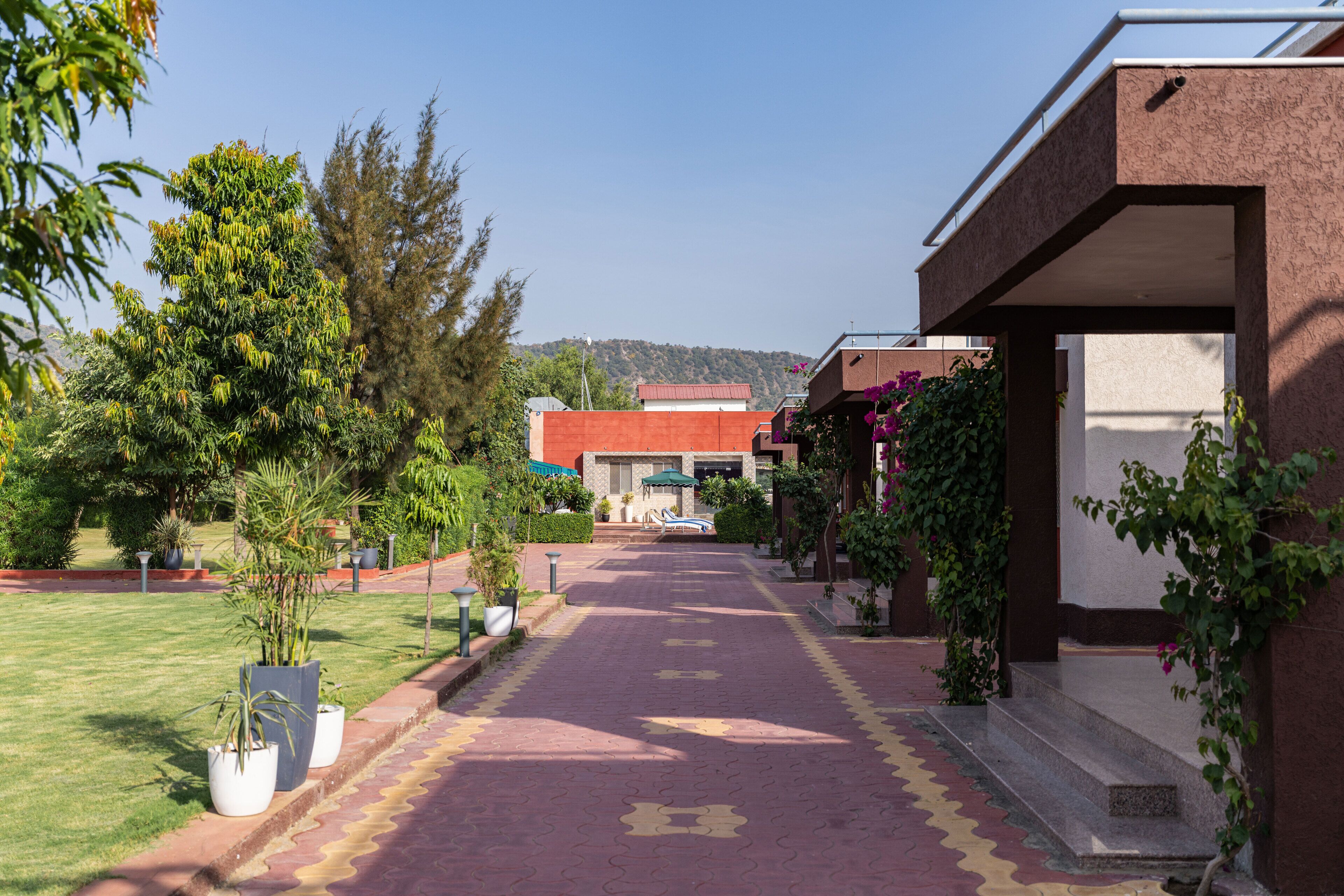 A pathway leading to a building with a red roof, surrounded by greenery and potted plants.