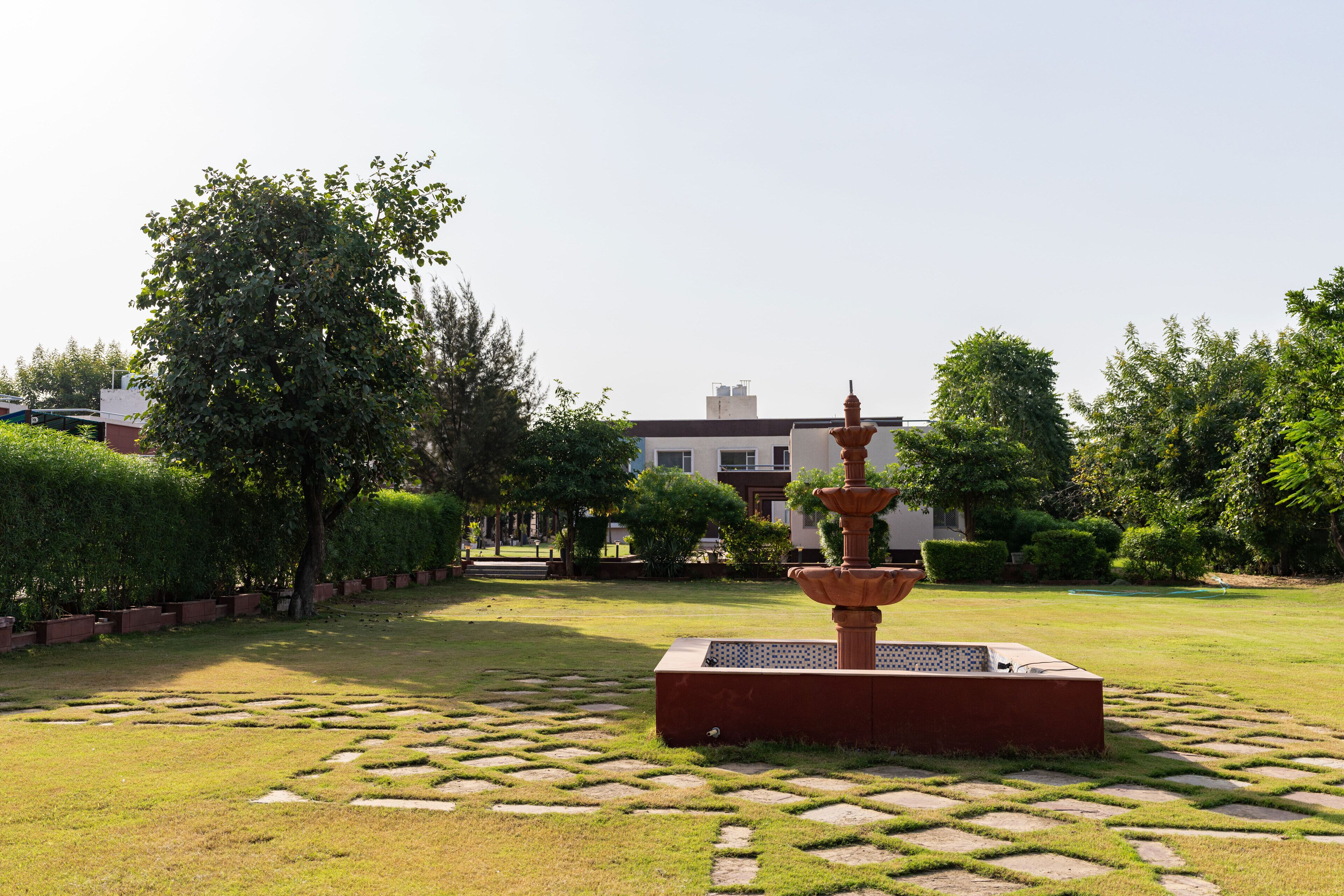 Un jardín con una fuente central, setos cuidadosamente recortados y un edificio al fondo.