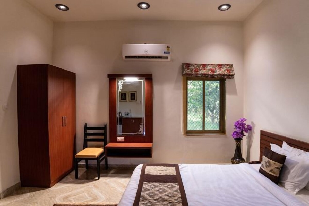 Un dormitorio con cama, armario, silla, tocador con espejo y ventana con vista a árboles.