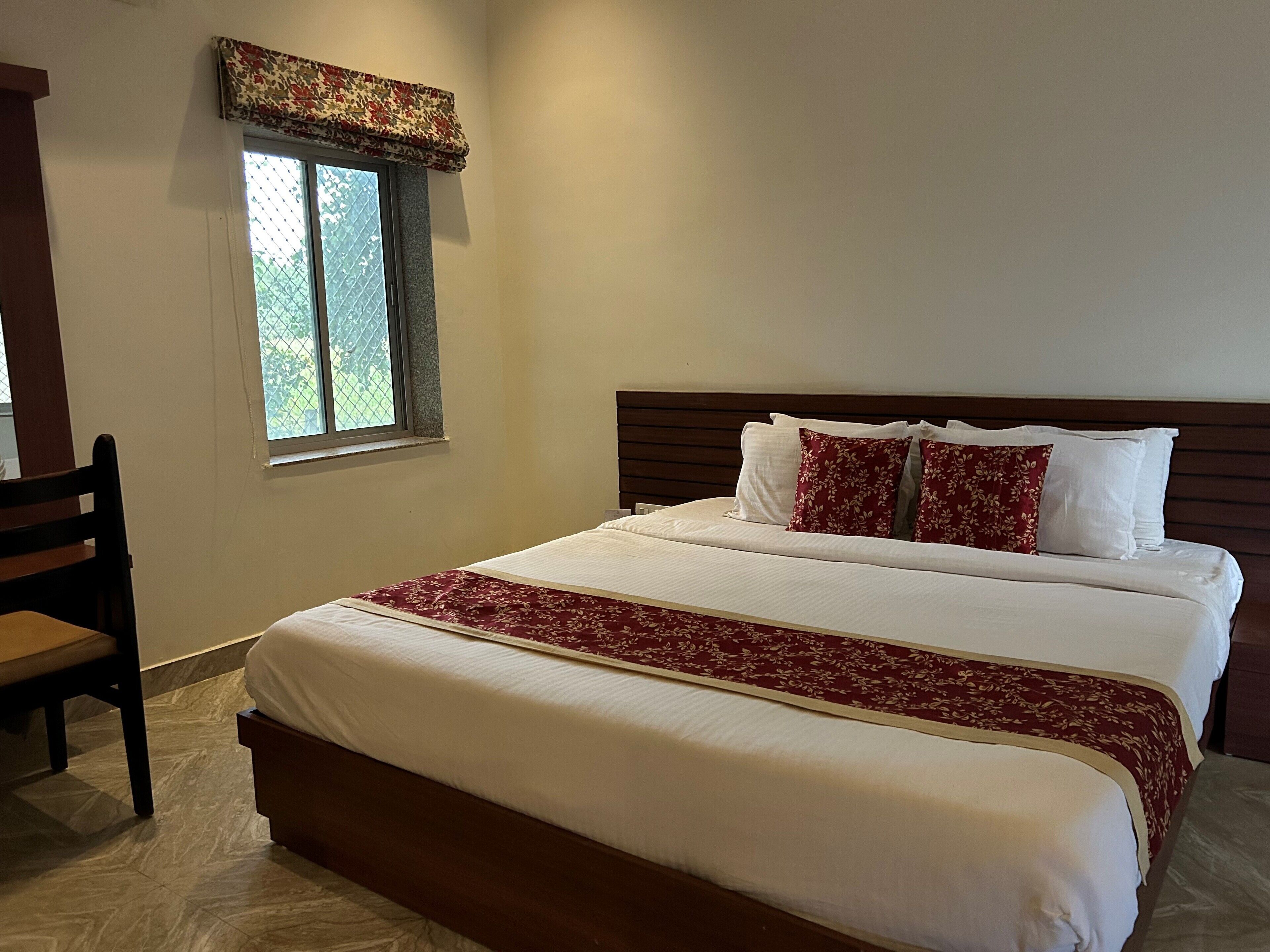 A neatly made bed with white and red bedding, a wooden headboard, and a window with a patterned valance.