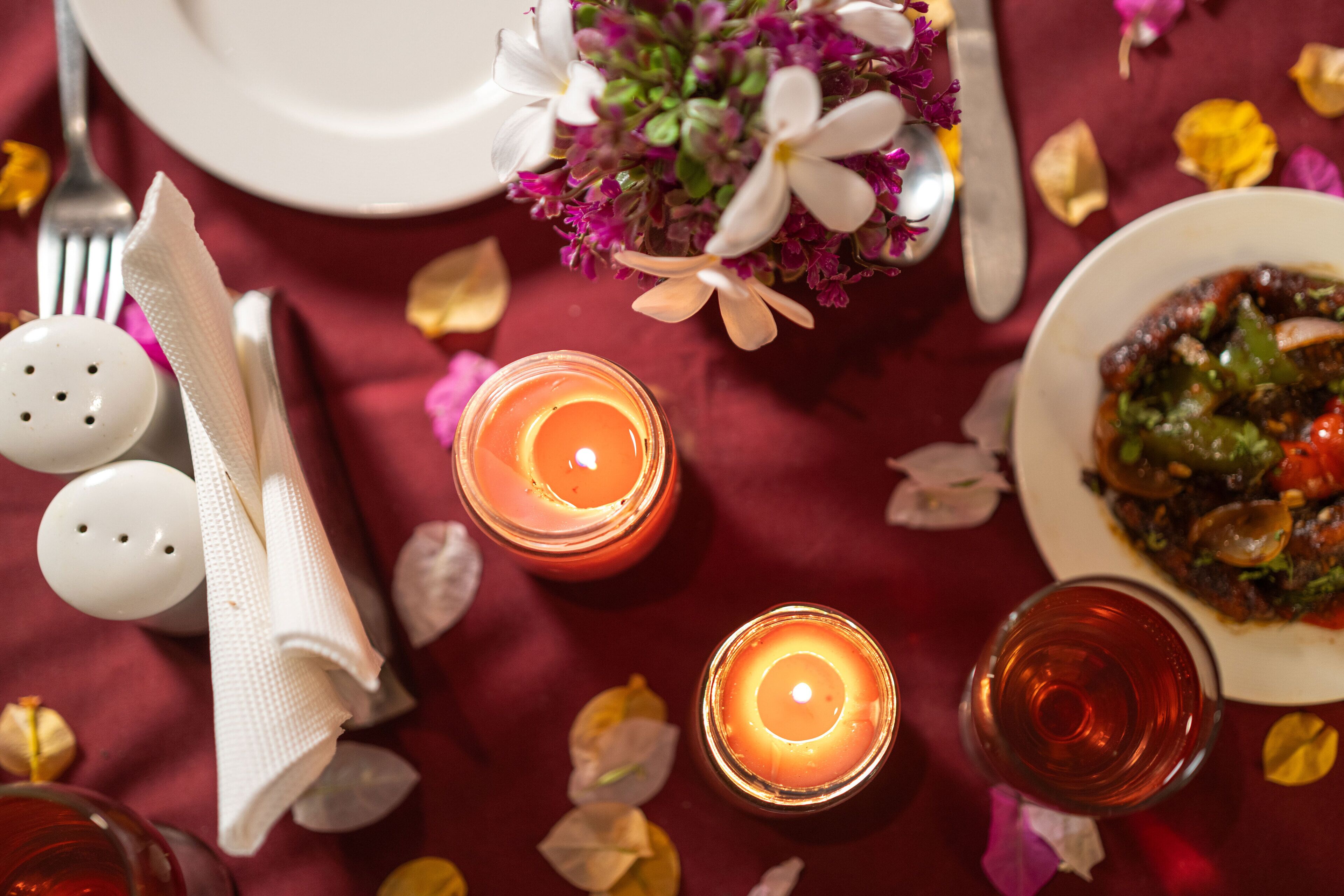 A table set with candles, a plate of food, and a vase of flowers.
