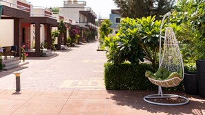 Una silla colgante con cojín verde en un jardín con plantas en macetas y un sendero empedrado.