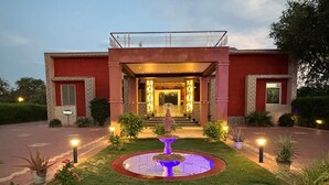 Entrada de hotel con una fuente central, fachada de edificio rojo y un camino bien iluminado.