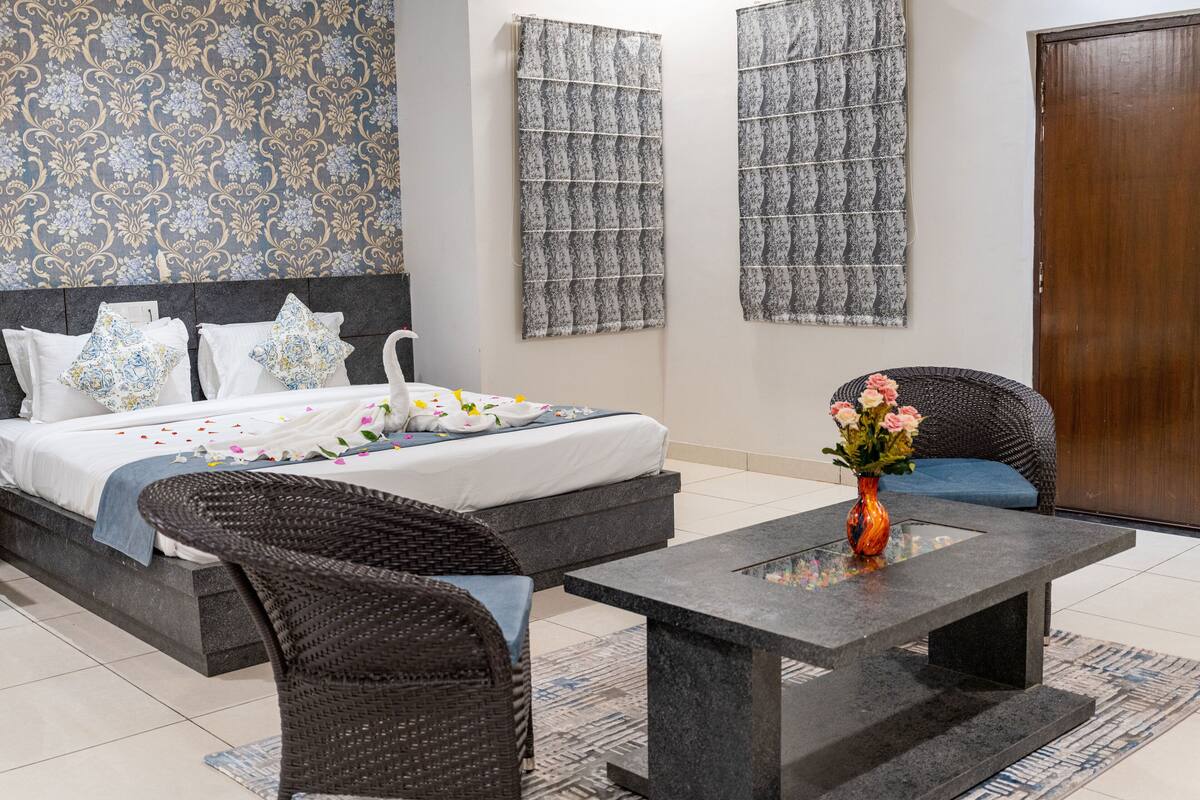 A bedroom with a bed, two wall-mounted curtains, a wicker chair, a stone coffee table, and a vase with flowers.