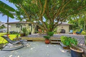 A patio area with a wooden deck, a large tree providing shade, and outdoor furniture including a lounge chair and a table. - Bonita Springs Oasis w/ Wooden Deck & Grill! (Bonita Springs)