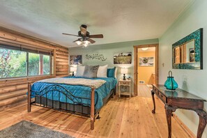 A log cabin bedroom with a bed, wooden floor, ceiling fan, and artwork on the walls. - Serene Driggs Cabin ~ 10 Mi to Grand Targhee! (Driggs)