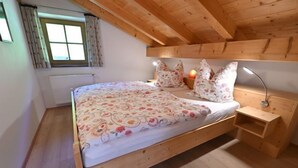 Un lit en bois recouvert d’une couvre-lit à motifs floraux, une table de chevet avec une lampe et une fenêtre avec des rideaux.