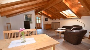 Une pièce chaleureuse avec un plafond en bois, une table à manger agrémentée d’un vase de fleurs, un canapé et une petite table.