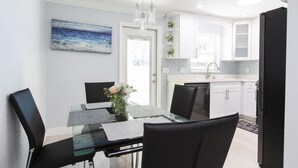A modern kitchen with white cabinets, a black refrigerator, and a dining area with a glass table and black chairs.