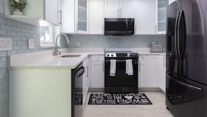 A modern kitchen with white cabinets, a stainless steel refrigerator, a microwave, and a stove.