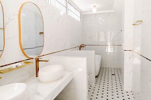 A modern bathroom with white marble walls, a large oval mirror, a gold faucet, and a black and white patterned floor. - Rose Apple Hotel (Bangkok)