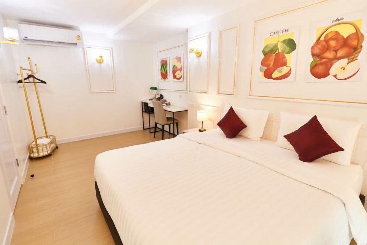 Une chambre d’hôtel avec un grand lit, un bureau et une chaise. Des tableaux encadrés ornent le mur et un panier est posé sur le sol.