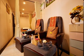 A massage room with two massage chairs, a small table with towels and a bottle of lotion, and a vase with flowers on a dresser. - Rose Apple Hotel (Bangkok)