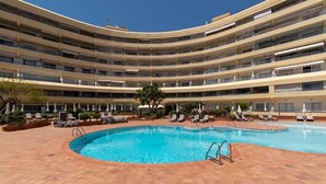 Ein mehrstöckiges Hotel mit einem zentral gelegenen Schwimmbecken, umgeben von Liegestühlen und Sonnenliegen.
