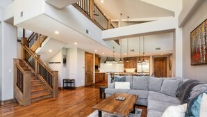 A spacious living area with a wooden staircase, a gray sectional sofa, and a wooden coffee table. - Bel Lago #7 · Impeccable Lakeside Penthouse - Pool & Hot-Tub, A/C (Avon)