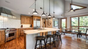 A spacious kitchen with wooden cabinets, a large island with bar stools, stainless steel appliances, and pendant lighting. - Bel Lago #7 · Impeccable Lakeside Penthouse - Pool & Hot-Tub, A/C (Avon)