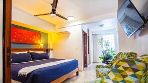 A bedroom with a bed, a ceiling fan, a wall-mounted TV, and a view of a balcony with plants.