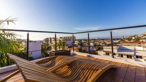 A rooftop terrace with a wooden hammock, potted plants, and a view of the cityscape.
