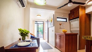 A dining area with a table set for two, a vase of flowers, and a kitchen with wooden cabinets and appliances.