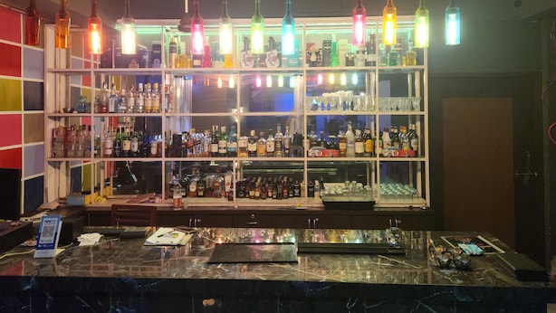 Uma área de bar com prateleiras cheias de garrafas de bebidas, bancada de mármore e luminárias pendentes.