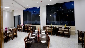 Uma ampla sala de jantar com uma mesa comprida posta para vários convidados, grandes janelas oferecendo vista do céu noturno e luminárias modernas.