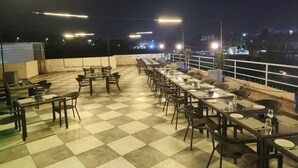 Um restaurante no terraço com piso xadrez, várias mesas e cadeiras, e iluminação externa.