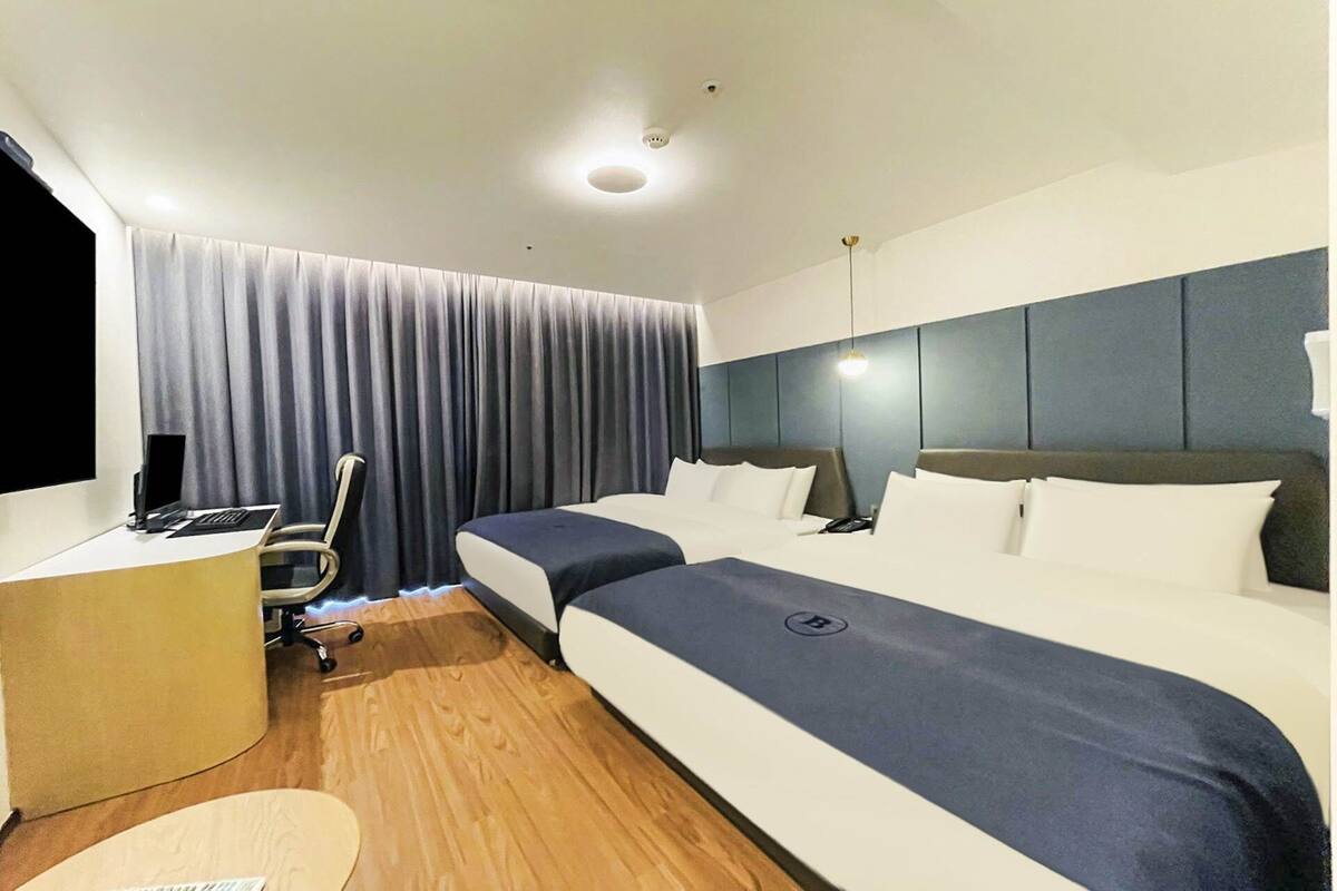 A hotel room with a bed, desk, chair, and curtains.