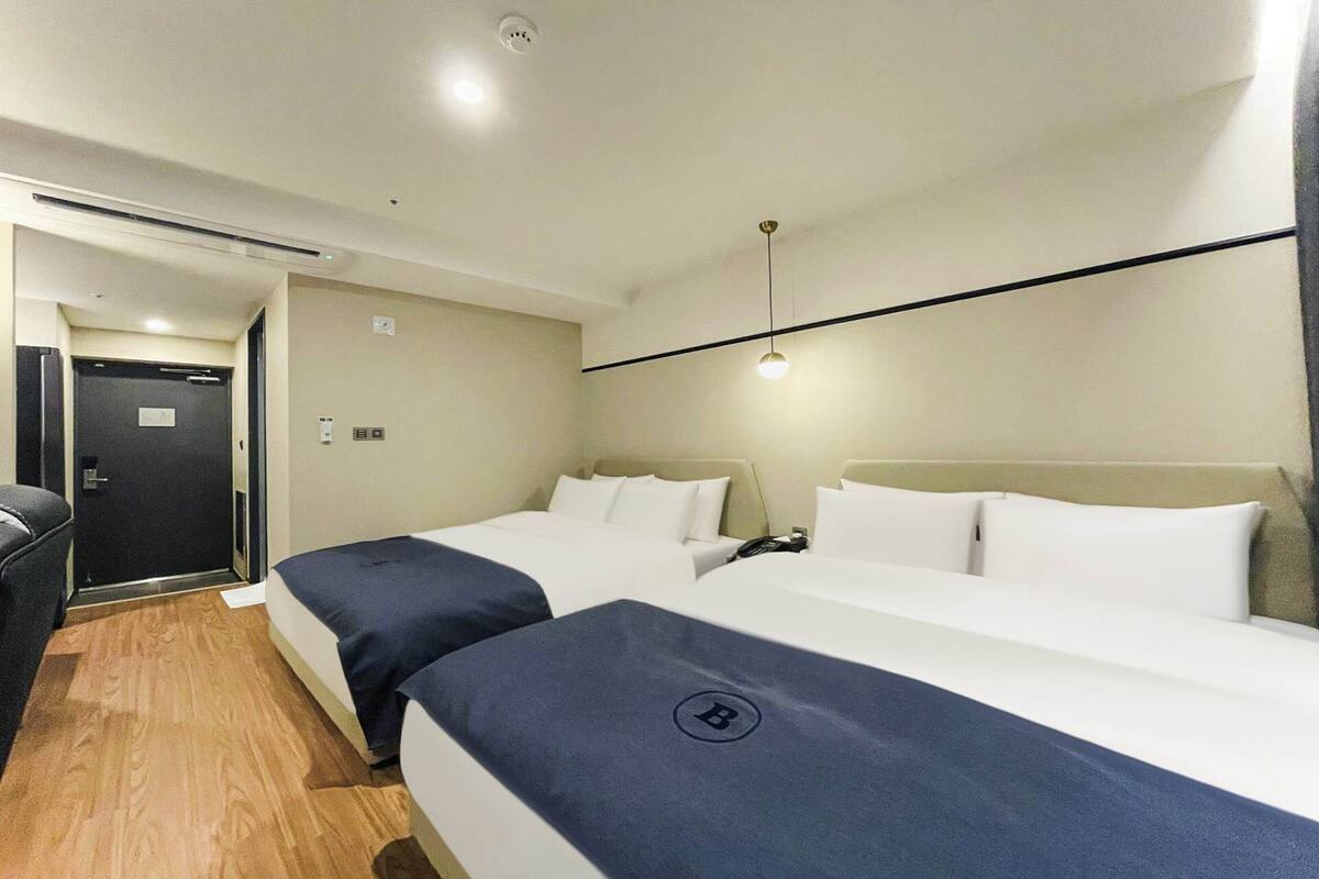 A hotel room with two beds, a desk, and a door.