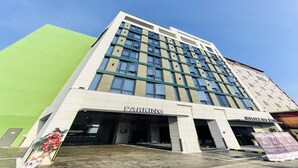 A multi-story hotel with a parking entrance, a green wall to the left, and a sign for a nearby restaurant. - Browndot Hotel (Yangsan)