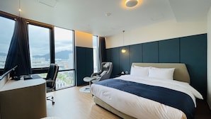A modern hotel room with a large bed, a desk with a computer, a chair, and a view of the city through large windows. - Browndot Hotel (Yangsan)