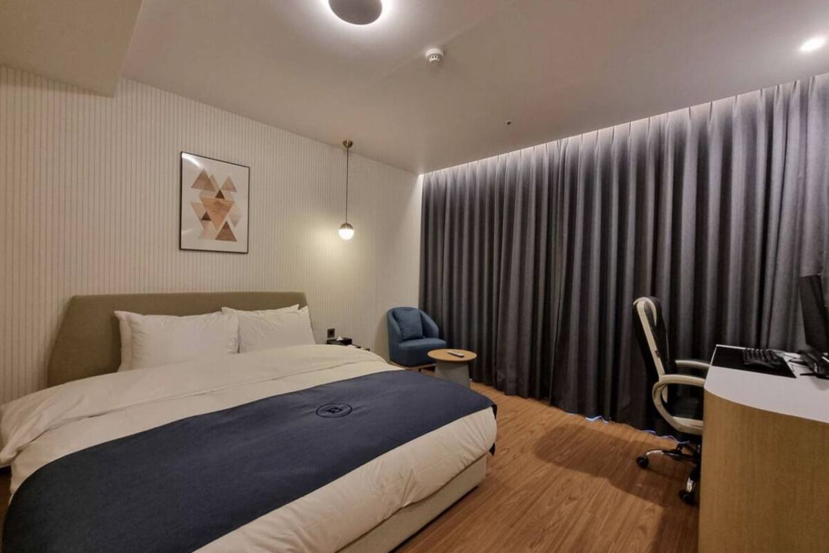 A hotel room with a large bed, a desk, a chair, and a curtain.