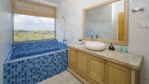 A bathroom with a large window, a bathtub, a sink, and wooden cabinets. - The Manor Hoi An Villa (Da Nang)