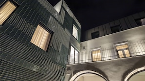 A modern building with a dark facade, large windows, and a balcony with a railing.