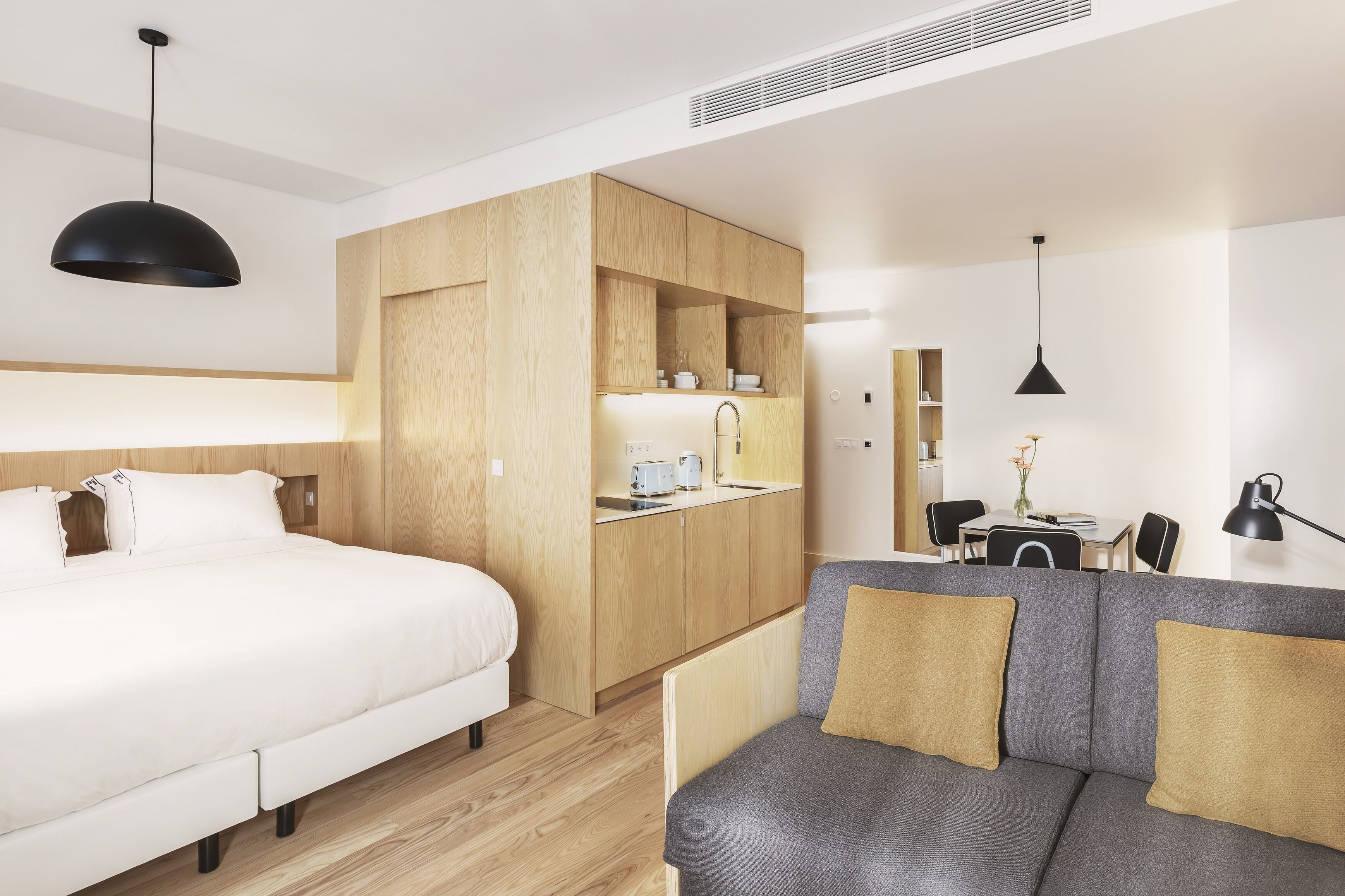 A modern hotel room with a bed, a sofa, a kitchenette, and a dining area.