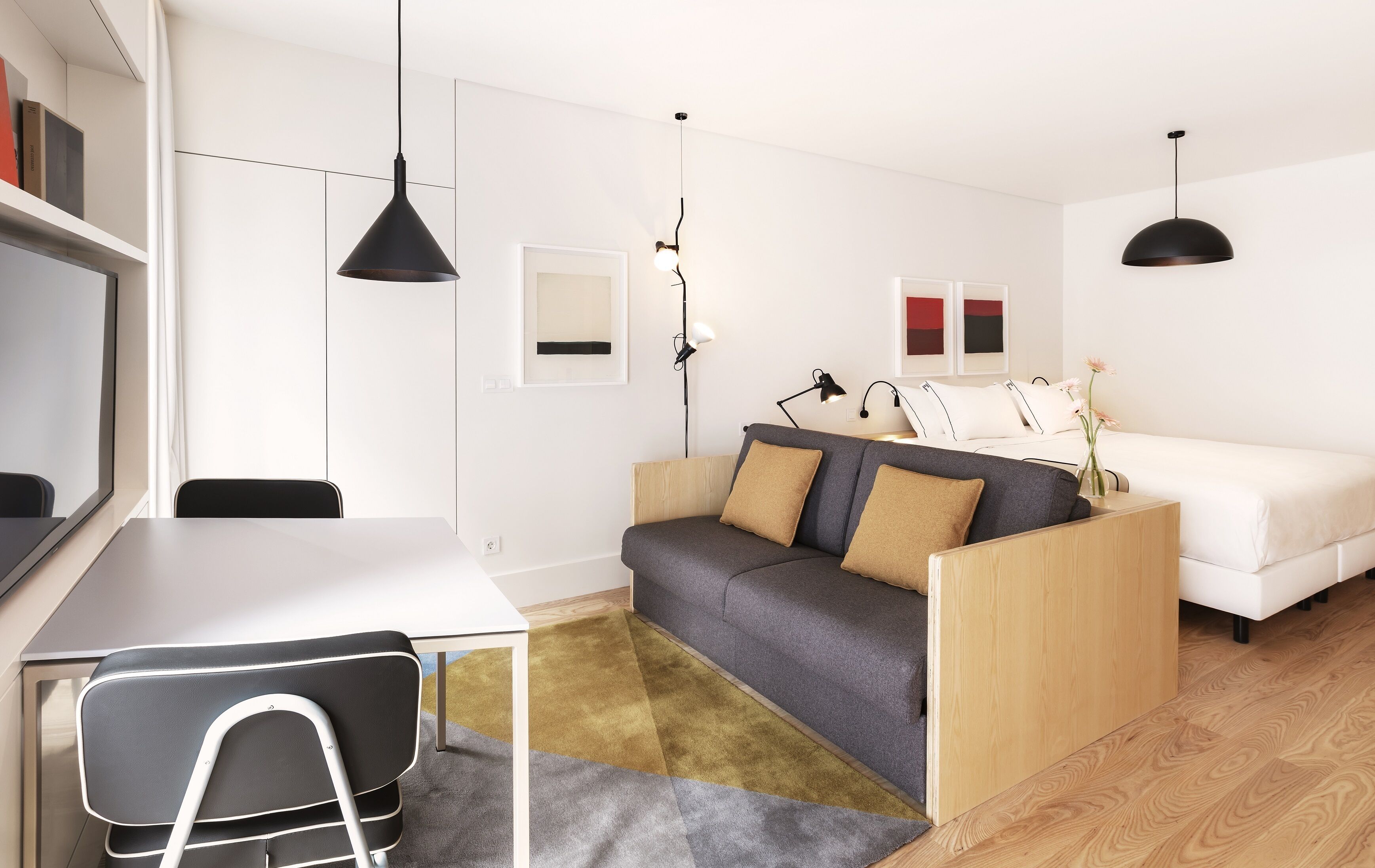 Ein modernes, minimalistisches Wohnzimmer mit einer Couch, einem kleinen Tisch und einem Sessel. Zwei Pendelleuchten und eine Stehlampe sind vorhanden.