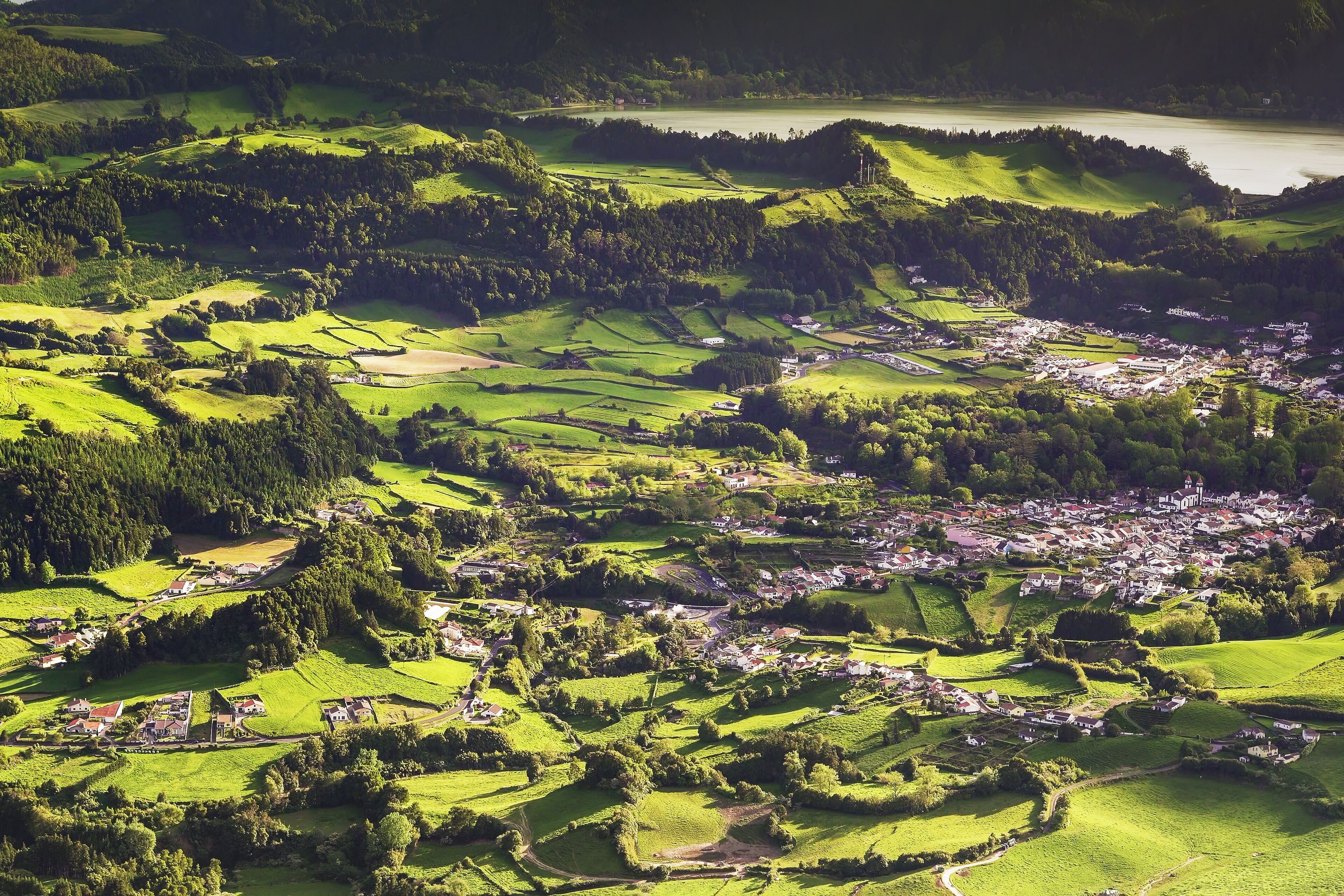 An aerial view of a rural village with terraced fields, a church, and a small body of water.