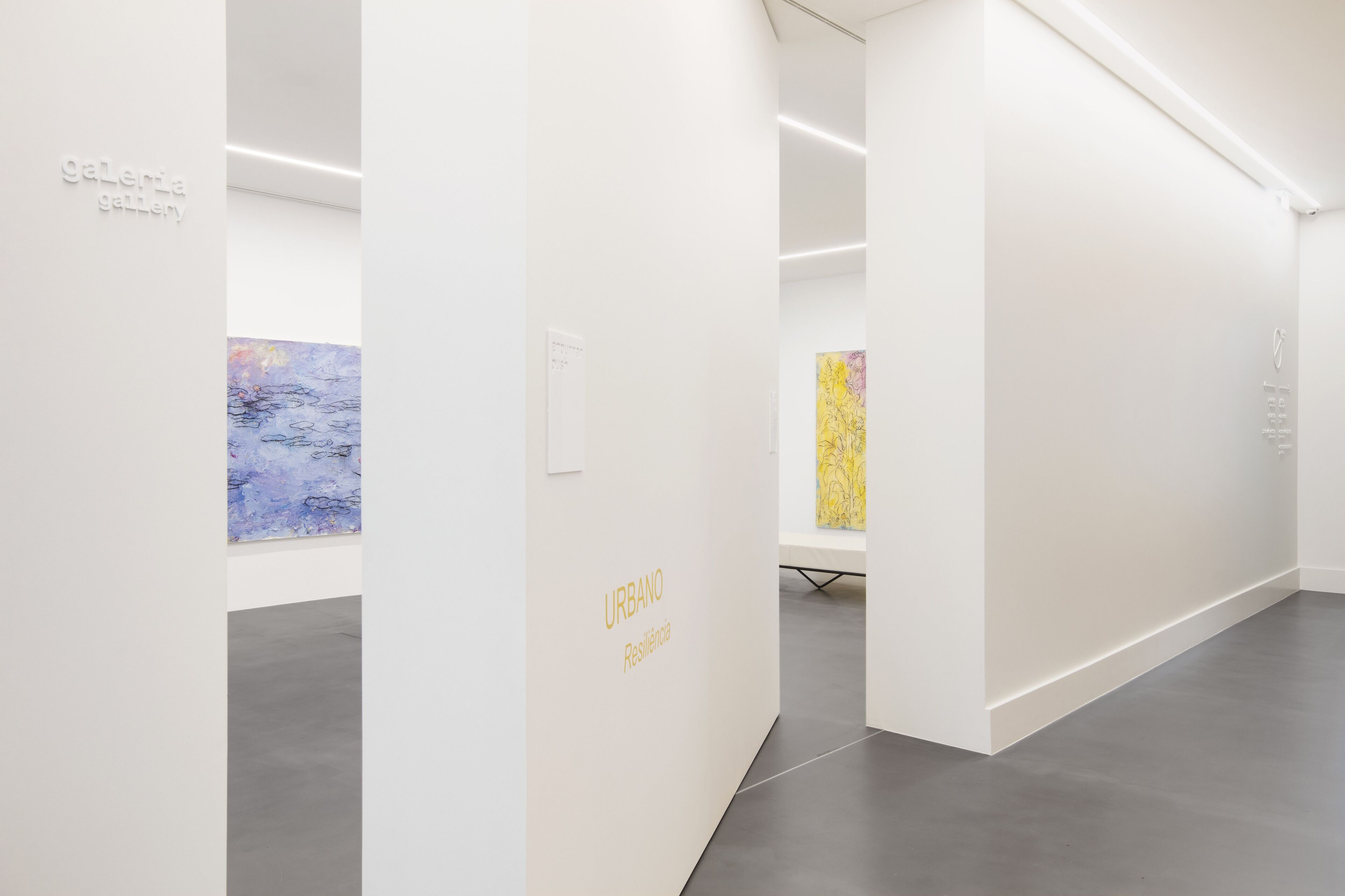 L’intérieur d’une galerie d’art, avec des murs blancs, un sol gris et des œuvres d’art exposées sur les murs.