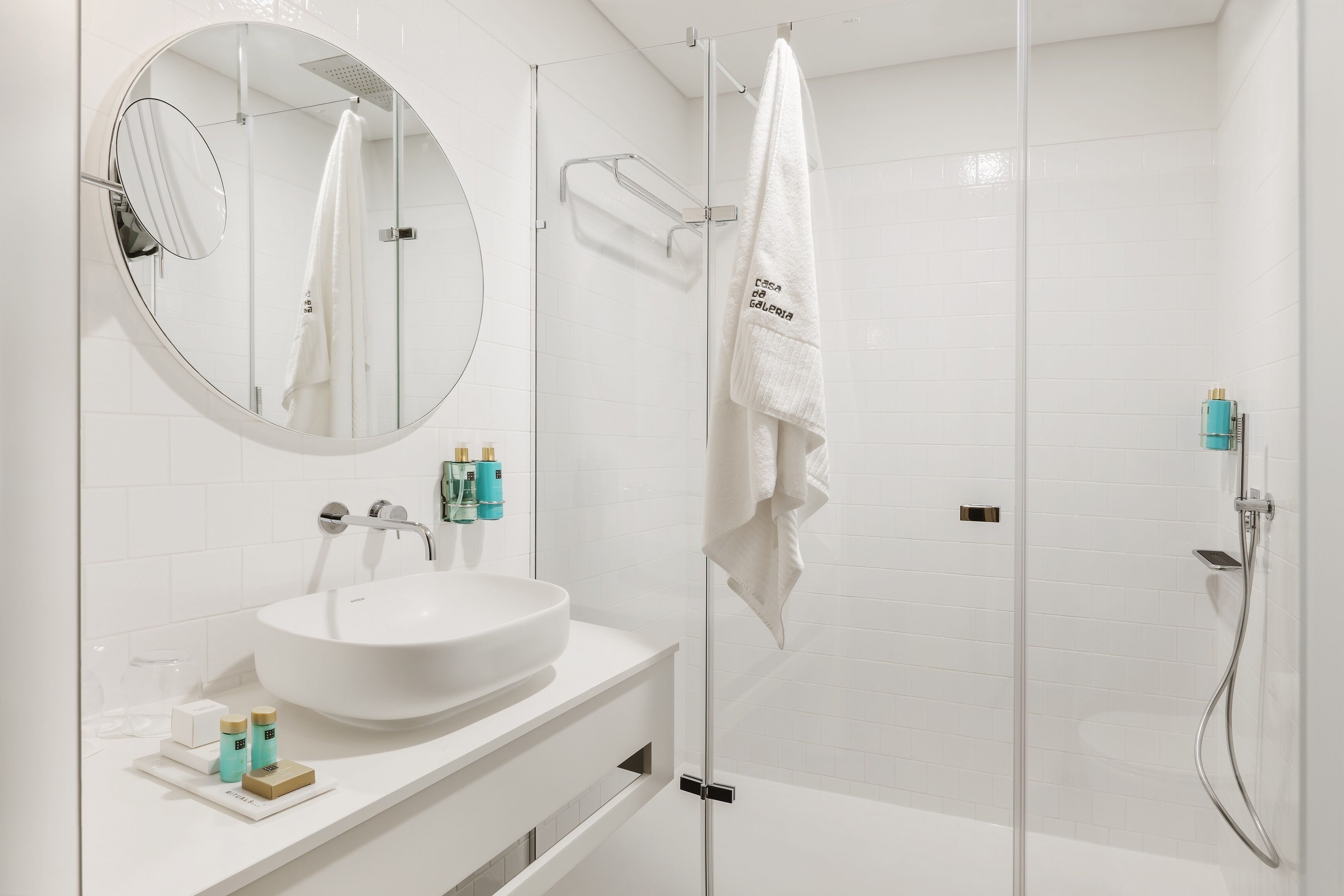 A modern bathroom with a round mirror, a white sink, and a glass-enclosed shower area.