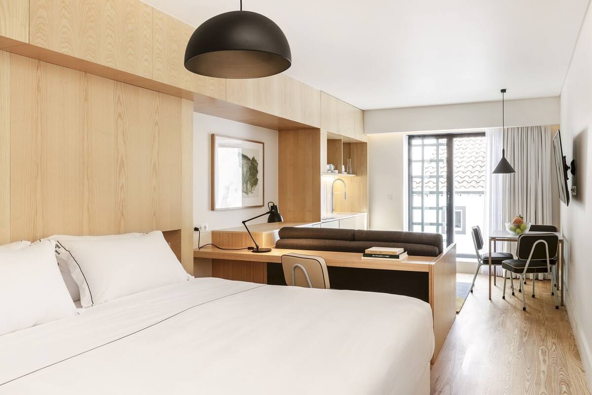 A hotel room with a bed, desk, chair, and a dining area with a table and chairs.