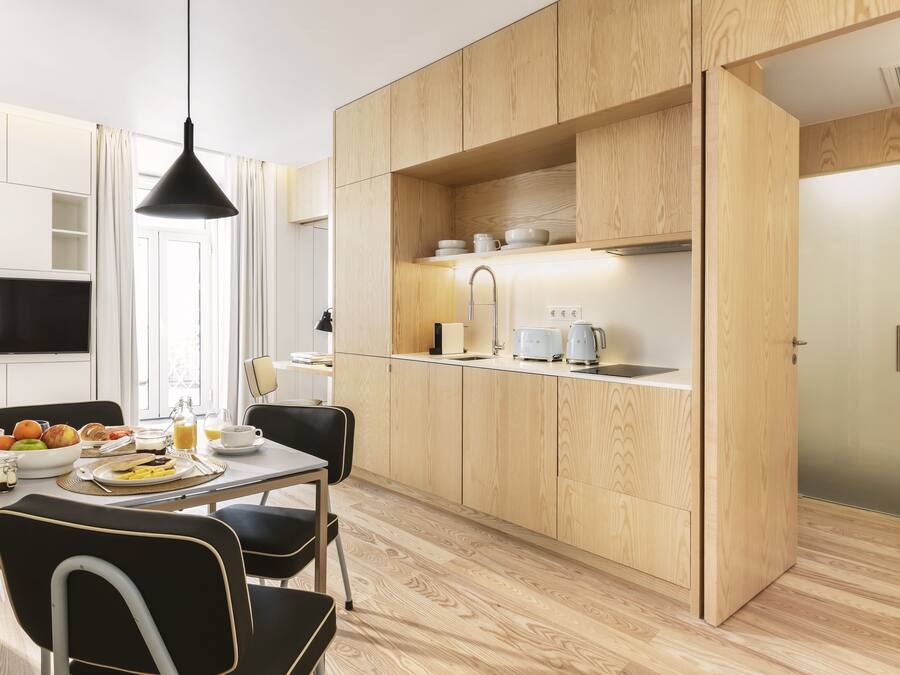 A modern kitchen with wooden cabinets, a dining table with chairs, and a breakfast setup.