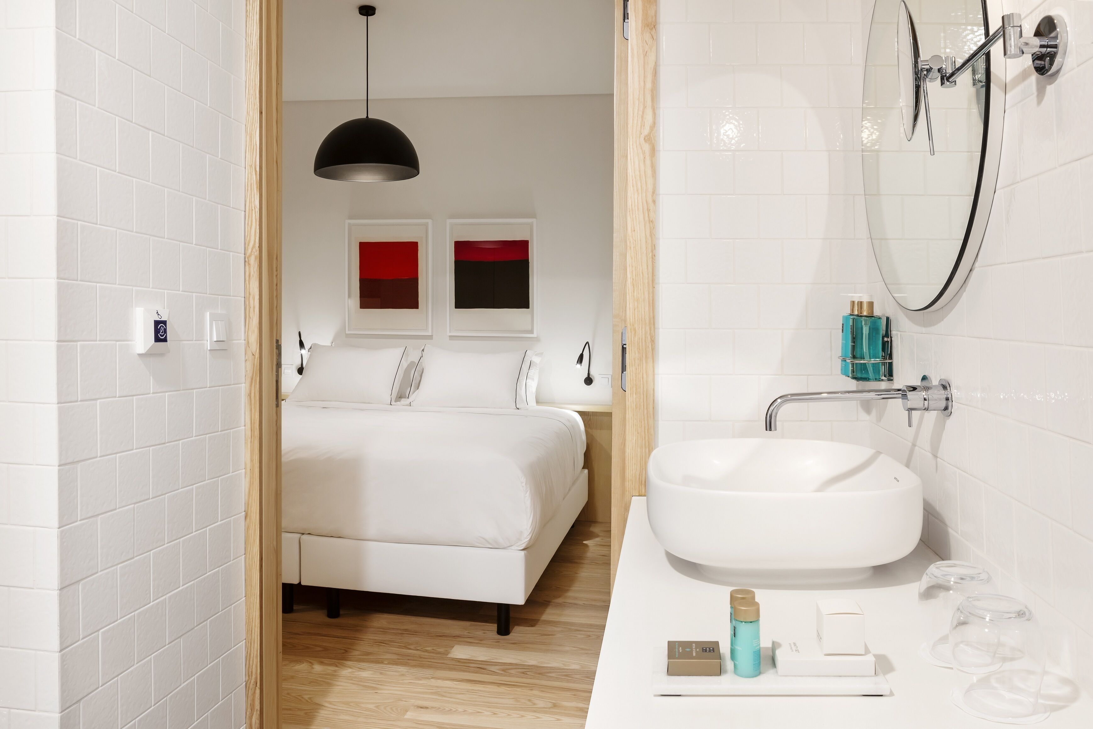 A modern bathroom with a white sink, a shower, and a bed in the background.
