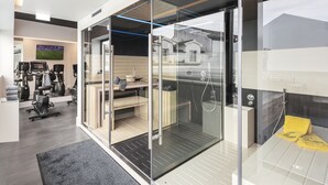 A modern gym with exercise equipment, a television, and a glass wall overlooking a residential area.