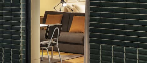 Una habitación con vistas a través de una ventana, un sofá, una silla y una lámpara.